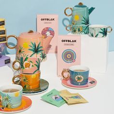 an assortment of coffee cups and saucers on a table with books, magazines and other items