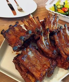 some ribs are on a white plate next to a salad