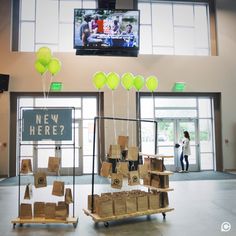 boxes and balloons are on display in front of a large television screen that reads new here?