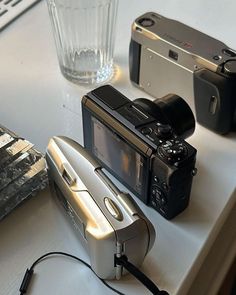 two cameras sitting on top of a white table next to a glass and silver object