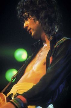 a man with no shirt on holding a guitar in his right hand and looking down at the ground