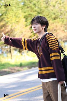 a young man points at something while standing on the side of the road in front of trees