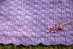 a knitted blanket laying on the ground with flowers in front of it and grass behind it