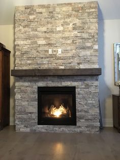 a fire place in a living room with wood flooring and a stone fireplace mantel