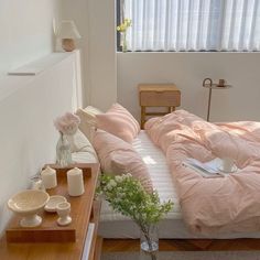 a bed with pink sheets and pillows in a room next to a table with flowers on it