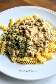 a white plate topped with pasta covered in mushroom gravy and garnished with herbs