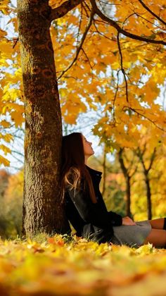 a woman is sitting under a tree in the fall leaves and looking up at the sky