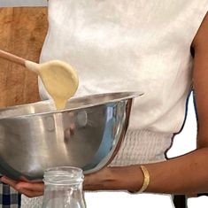 a woman holding a metal bowl with a wooden spatula in it and mixing ingredients