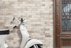 a white scooter parked in front of a brick wall with a door behind it