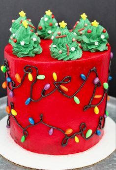 a red cake with green frosting and christmas lights on it's top is sitting on a plate