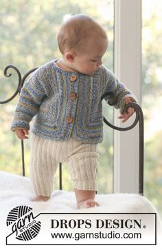 a baby standing on top of a bed next to a window