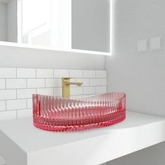 a red glass bowl sitting on top of a white counter next to a bathroom mirror