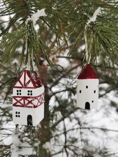 two white and red houses hanging from a pine tree with snow on the branches behind them