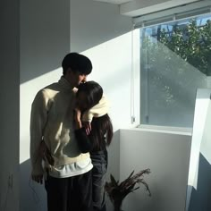 two people standing next to each other in front of a window with the sun shining through