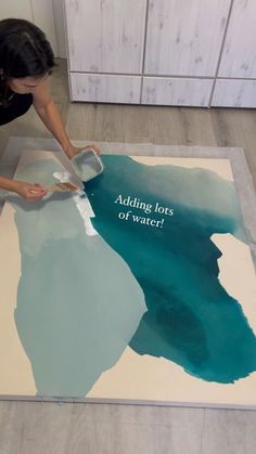 a woman is painting on the floor with blue and white paint that says adding less of water