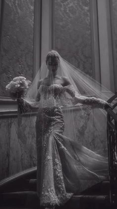 a woman in a wedding dress and veil standing next to a window with flowers on it