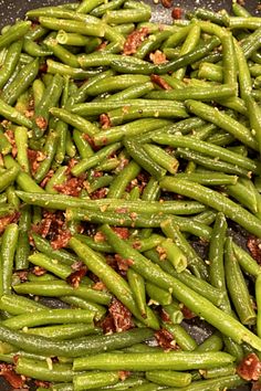 green beans are being cooked in a frying pan with bacon on the side and seasonings