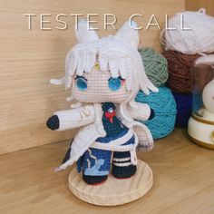 a crocheted doll sitting on top of a wooden table next to balls of yarn