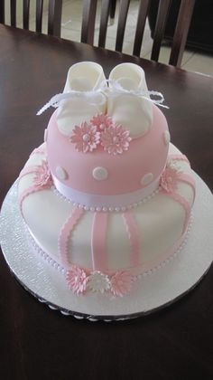 a pink and white cake with baby shoes on the top is sitting on a table