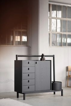 a black and grey cabinet with drawers in an empty room next to a wooden chair