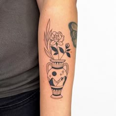 a woman with a tattoo on her arm has a vase with flowers and leaves in it