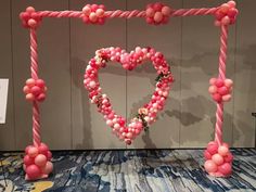 a heart shaped balloon frame with pink and white balloons attached to the top, on a carpeted floor