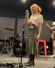 a woman standing in front of a microphone on top of a stage with other instruments