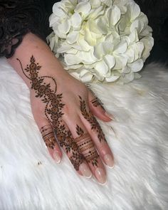 a woman's hand with henna tattoos on it and flowers in the background