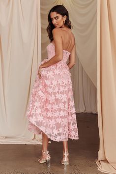 a woman wearing a pink dress standing in front of curtains with her back to the camera