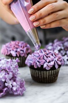 a woman is decorating cupcakes with purple frosting and flowers on them