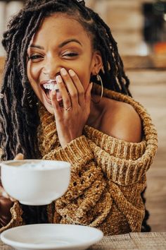 a woman sitting at a table with a cup of coffee and eating something in front of her