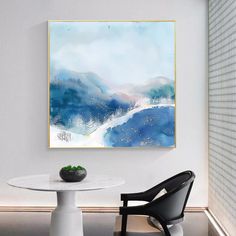 a painting hanging on the wall next to a table with a chair and potted plant