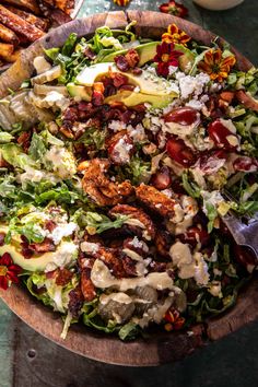 a salad in a wooden bowl with dressing on top and other food items around it