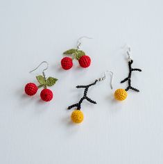 three crocheted fruit earrings are shown on a white surface, one is red and the other is yellow