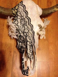 a cow's skull is adorned with lace and beaded beads on a wooden floor