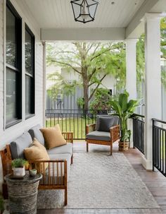 a porch with two chairs and a couch on the front porch next to a tree