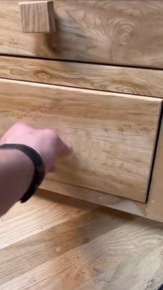 a person is opening the drawer on a wooden dresser with their hand and black rubber band