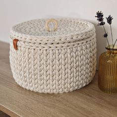 a white knitted basket sitting on top of a wooden table next to a vase