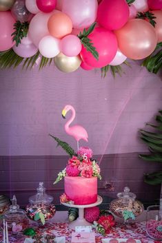 a pink cake with a flamingo on top and balloons in the air above it