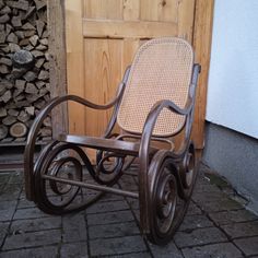 a wooden rocking chair sitting on top of a brick floor next to a pile of firewood