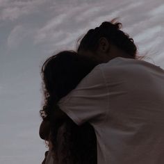 a man and woman embracing each other in front of a sky with clouds behind them