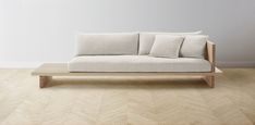 a couch sitting on top of a wooden floor next to a white wall with three pillows