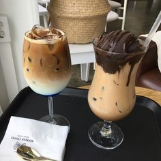 two drinks are sitting on a tray with spoons next to each other, one has chocolate and the other has ice cream