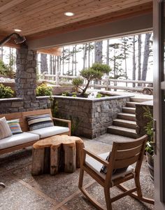 an outdoor living area with wooden furniture and stone steps leading up to the deck, surrounded by pine trees