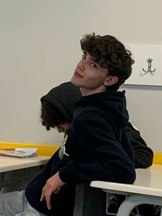 a young man sitting at a desk with his head turned to the side, looking off into the distance