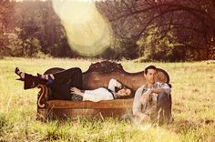 two people are laying on an old couch in the middle of a field with trees