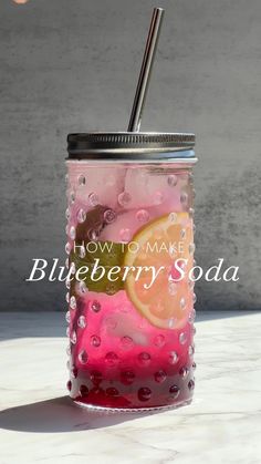 a mason jar filled with pink and yellow liquid next to a metal straw in front of a concrete wall