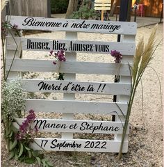 a wooden sign sitting on top of a gravel ground next to grass and flowers in front of a building