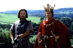 two men dressed in medieval clothing standing next to each other on top of a hill