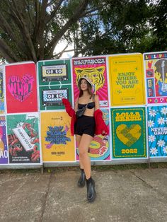 a woman standing in front of a wall with posters on it's sides and trees behind her